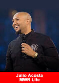 Julio Acosta speaking on stage at an MWR Life event, holding a microphone and smiling.