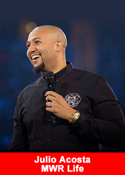 Julio Acosta speaking on stage at an MWR Life event, holding a microphone and smiling.